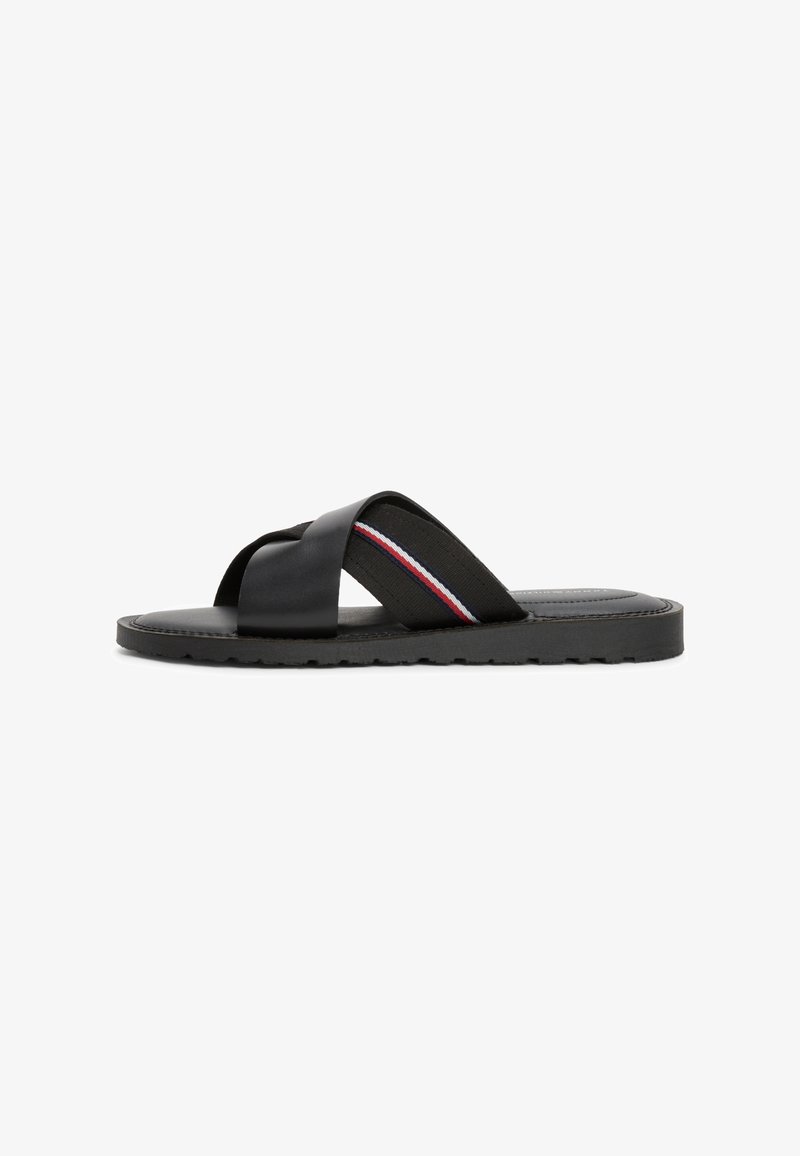 Black sandal with crisscross straps, made of smooth leather and elastic fabric featuring a red, white, and blue stripe, textured sole.