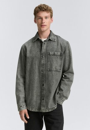 Gray denim shirt with a button-up front, collar, and one chest pocket. Features contrasting stitching and a relaxed fit. Textured fabric.