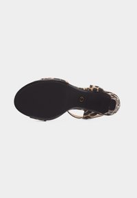 Sandale à imprimé léopard avec semelle noire, bride à la cheville, petit talon bloc et boucle dorée, vue de dessous.