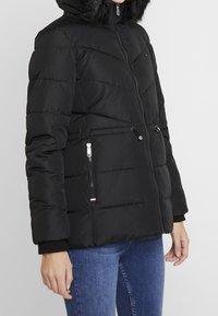 Chaqueta negra tipo puffer con cremallera frontal, capucha y ribete de piel sintética. Cuenta con bolsillos laterales, puños elásticos y textura acolchada.