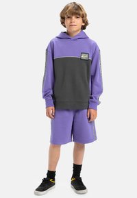 Hoodie violet et gris avec une poche avant, associé à un short violet. Présente des coutures contrastées et un patch logo sur la poitrine.