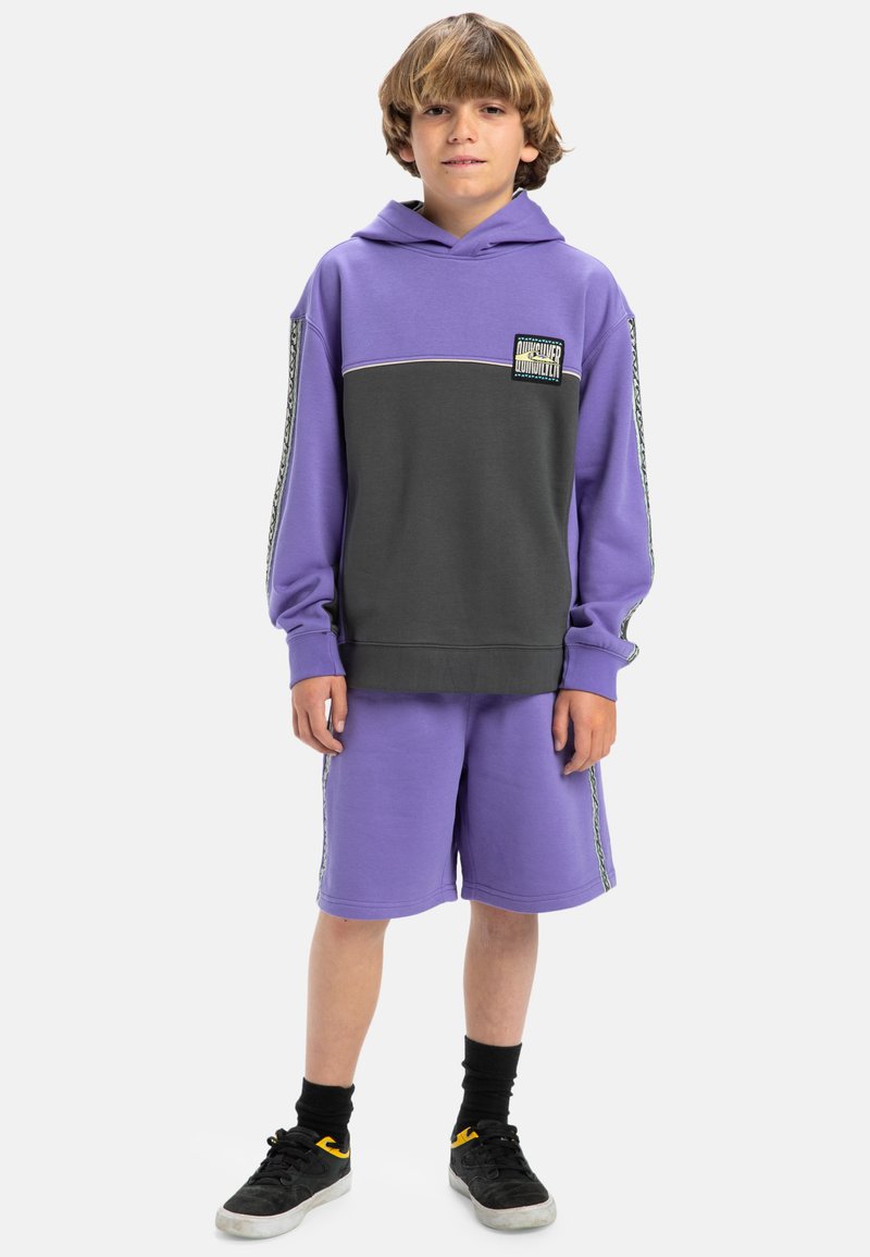 Hoodie violet et gris avec une poche avant, associé à un short violet. Présente des coutures contrastées et un patch logo sur la poitrine.