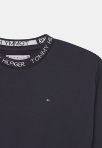 Ciemnoniebieska bluza z ribbowanym dekoltem typu crew, z napisem "TOMMY HILFIGER" oraz małym logo w kolorach czerwonym, białym i niebieskim na klatce piersiowej.
