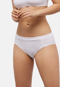 Braga blanca de algodón con textura suave, que presenta una cintura ancha y delicados bordes festoneados. Corte de tiro medio.