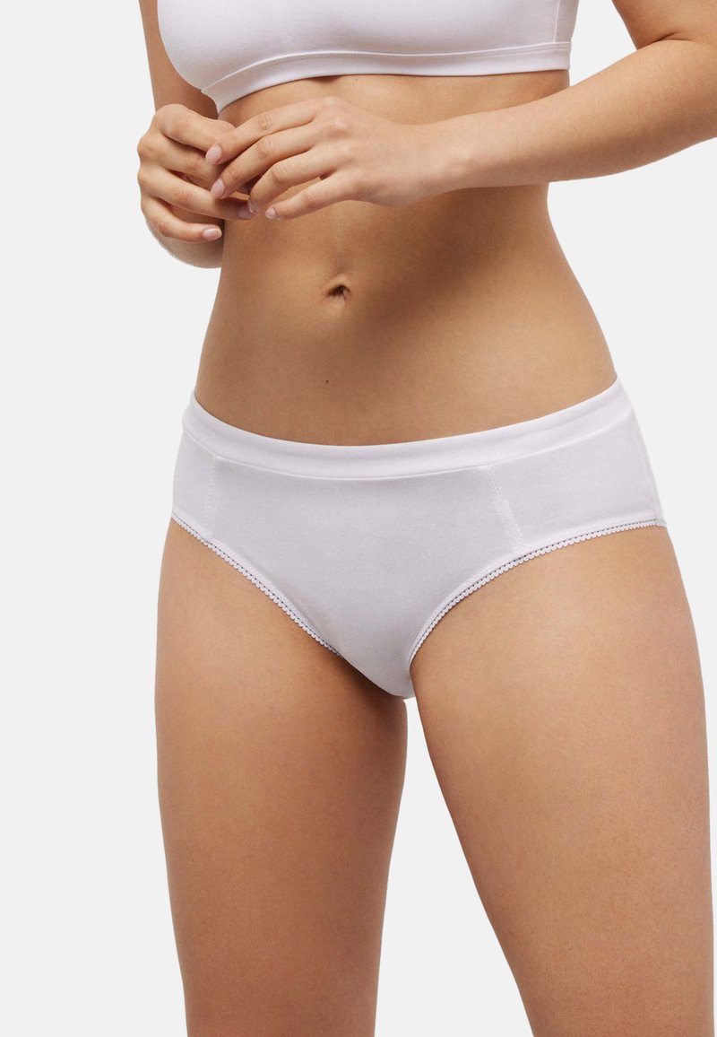 Braga blanca de algodón con textura suave, que presenta una cintura ancha y delicados bordes festoneados. Corte de tiro medio.