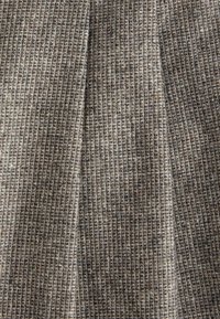 Gros plan sur un tissu texturé gris et brun avec un petit motif à carreaux et des détails de tissage visibles.