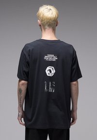 Μαύρο βαμβακερό T-shirt με στρογγυλή λαιμόκοψη, κοντά μανίκια και γραφικό εκτύπωση στην πλάτη με κείμενο και εξαγωνικό σχήμα.