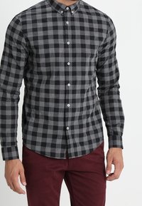 Zwart en grijs geruite knopshirt met lange mouwen, aangevuld met een ronde kraag en witte knopen, gedragen over maroon broeken.
