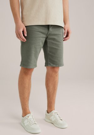 Shorts en coton verts avec une coupe droite, ourlets retroussés et coupe décontractée, accompagnés de baskets blanches avec un logo sur le côté.