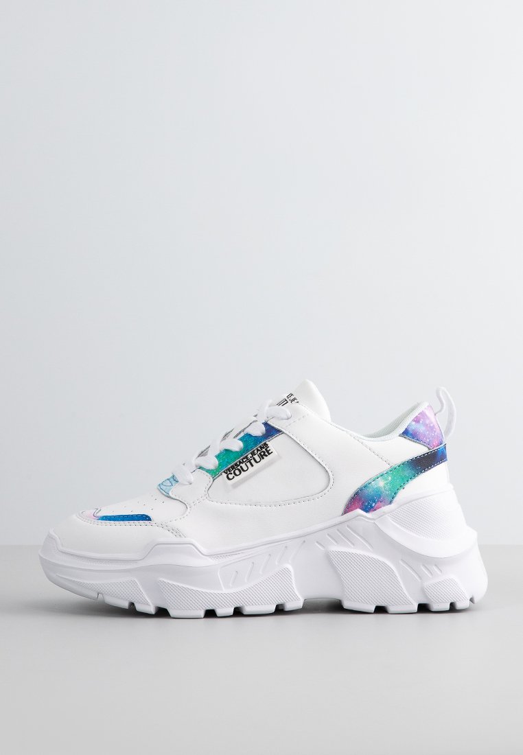 Zapatillas blancas con una suela gruesa, que presentan un acento iridiscente colorido en el talón y los lados, y una etiqueta de marca en el lado exterior.