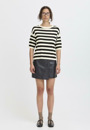 Top a maniche corte a righe bianche e nere abbinato a una mini gonna nera in pelle. Modello con calzini beige e scarpe nere. Design minimalista.