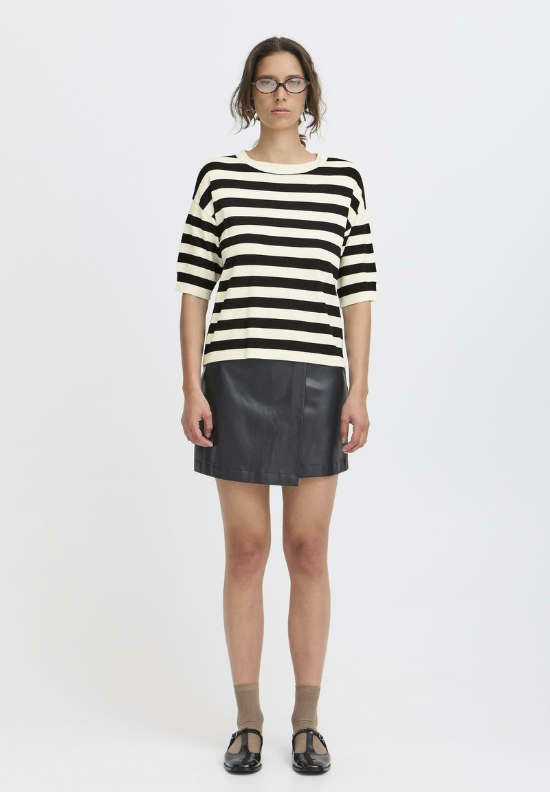 Top a maniche corte a righe bianche e nere abbinato a una mini gonna nera in pelle. Modello con calzini beige e scarpe nere. Design minimalista.