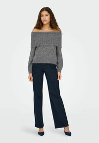 Pull gris à épaules dénudées avec texture côtelée, associé à un jean bleu foncé à jambes larges et des escarpins bleus à bout pointu. Matière tricotée.