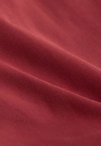 Vue rapprochée et lisse d’un tissu rouge montrant une texture fine et des plis doux créant des ombres douces.