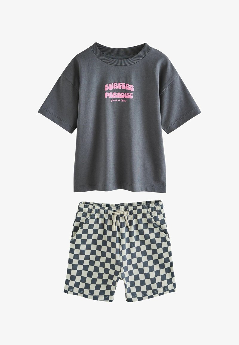 T-shirt gris foncé à manches courtes avec texte rose "SURFERS PARADISE Catch A Wave" et short à cordon noir et blanc à carreaux.