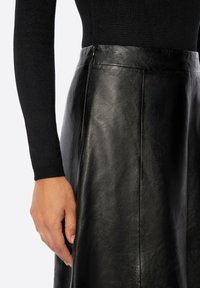 Jupe en cuir noir à la texture lisse, avec une taille ajustée et des détails de coutures discrètes, associée à un haut noir à manches longues.