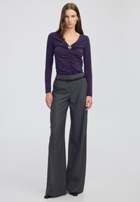 Fioletowa bluzka z długim rękawem, z marszczonym przodem i okrągłym detalem; zestawiona z szarymi, wysokim stanem spodniami z szerokimi nogawkami i czarnym paskiem.