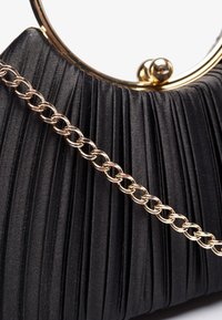 Sac à main en tissu noir plissé avec une structure en métal doré et une chaîne. Présente un fermoir arrondi et une texture lisse.