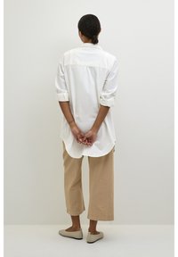 Camisa branca de botão com mangas arregaçadas, combinada com calças largas bege e sapatos claros. Design simples, textura suave.