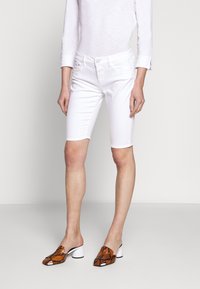 Bermudas de mezclilla blanca con cinco bolsillos, combinadas con mules de estampado de serpiente en naranja y negro y un tacón cuadrado blanco.