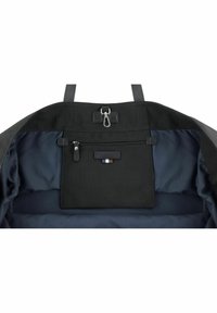 Intérieur de sac noir avec doublure marine, comprenant une poche zippée et un compartiment plat avec un accent en cuir. La quincaillerie inclut un fermoir à clip.