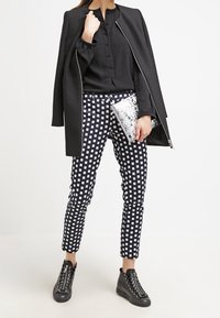 Blusa nera a maniche lunghe, con bottoni chiari, abbinata a pantaloni a scacchi bianchi e neri. Completato con un giubbotto nero e sneakers nere alte.