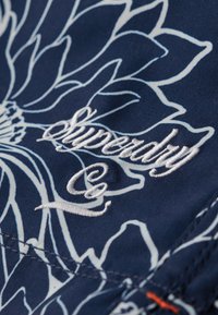 Marine stoffen met een wit bloemenpatroon; voorzien van het geborduurde "Superdry" logo in witte draad. Vlekkeloze textuur met contrasterende stikseldetails.