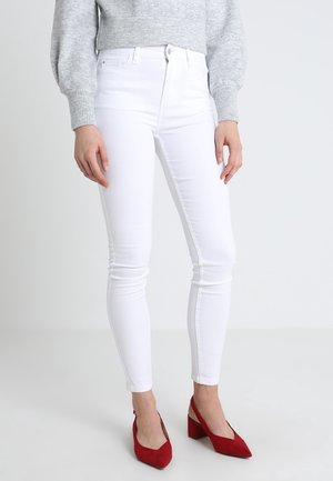 Vaqueros blancos ajustados de cintura alta, hechos de un tejido de algodón elástico. Combinados con un suéter gris y tacones de ante rojos. Textura suave.