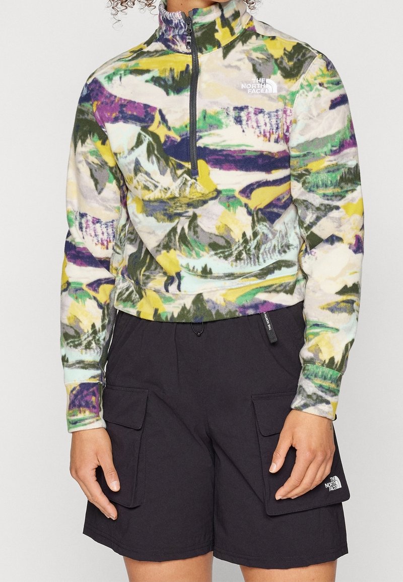 Fleece-pullover med ett flerfärgat bergsmönster, kvartslång dragkedja framtill, hög krage och logotyp på vänster bröst; kombinerat med svarta cargoshorts.