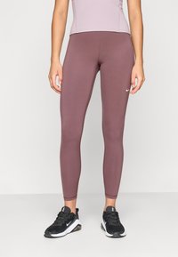 Leggings de rendimiento de Nike en un tono malva suave, tejido elástico con textura suave. Presentan un diseño ajustado, logo en la cadera y costuras a lo largo de las piernas.