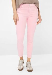 Jeans skinny rosa con una texture liscia, cinque tasche e chiusura con bottone. Abbinati a sneaker chiare con accenti rosa.