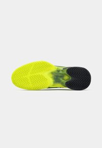 Sole tenisky Lacoste s rozděleným designem: jasně žlutá guma se zigzagovým vzorem a texturovaná černá guma s herringbone gripem.