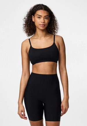 Svart sportsbra med tynne stropper, kombinert med høy-waisted svarte sykkelshorts. Glatt tekstur og tettsittende design. Enkelt og minimalistisk stil.