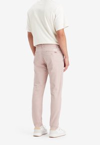 Ljusrosa byxor av mjukt tyg, med smal passform, bakfickor och en etikett nära midjan. Bärs med en vit kortärmad skjorta.