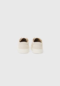 Sneakers in suede beige con design a basso profilo, suola in gomma bianca e dettagli cuciti. Presentano un'etichetta posteriore con marchio e uno stile minimalista.