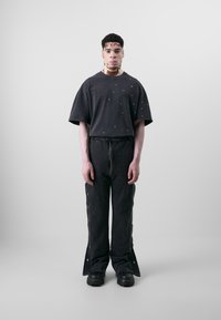 Mørkegrå oversized t-shirt med metalnitter, parret med matchende bredbenede bukser med lynlåse og trykknapdetaljer, afsluttet med støvler med grov sål.
