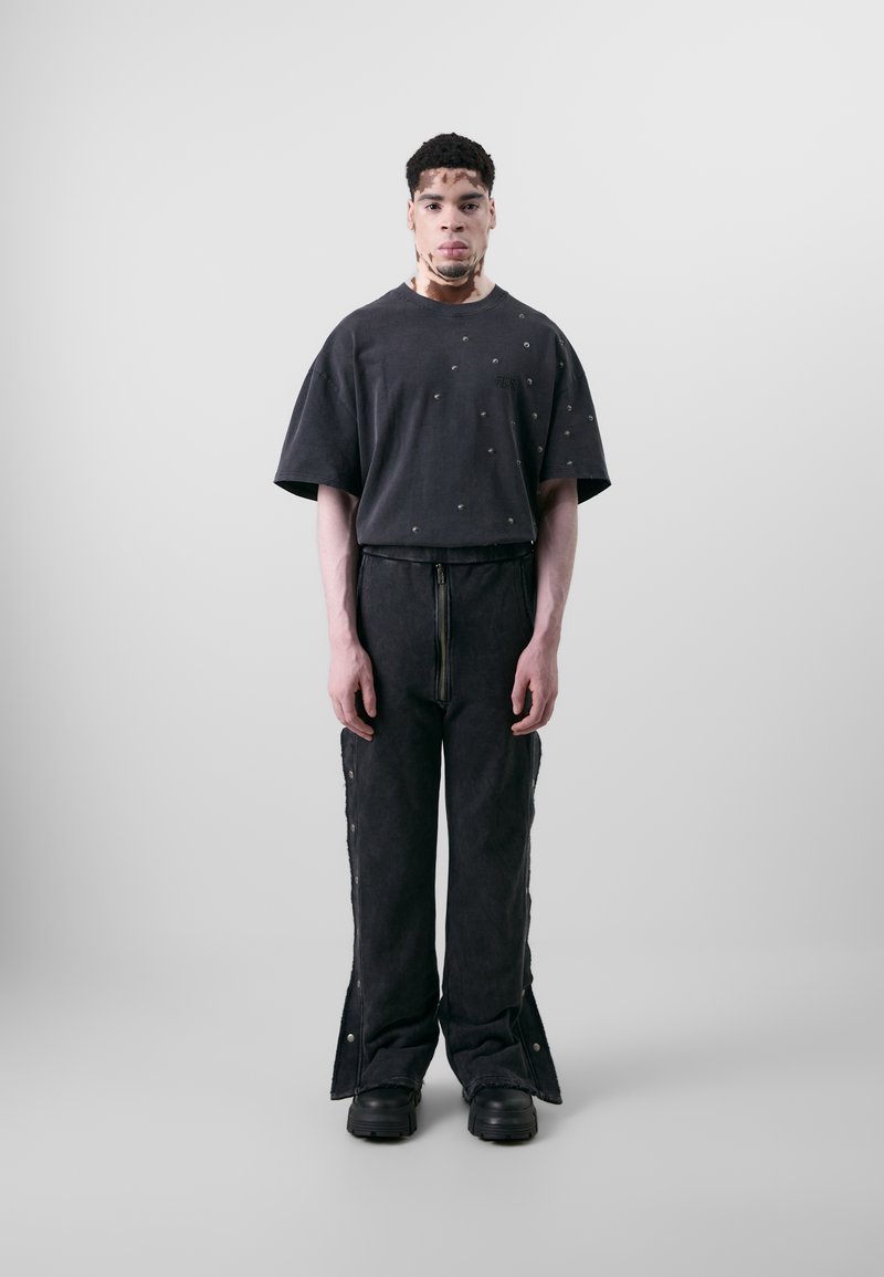 Mørkegrå oversized t-shirt med metalnitter, parret med matchende bredbenede bukser med lynlåse og trykknapdetaljer, afsluttet med støvler med grov sål.