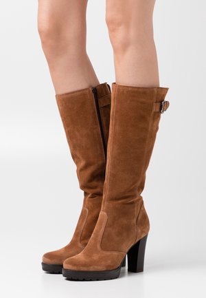 Ruskeat mokkanahkaiset polven yli ulottuvat saappaat, joissa on lohkokorko, sivuvetoketju ja solkikoriste, sileä pinta ja pyöreä varvas.