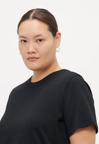 T-shirt nera a maniche corte in tessuto di cotone, con collo rotondo, vestibilità ampia e dettagli di cucitura discreti lungo la cucitura della spalla.