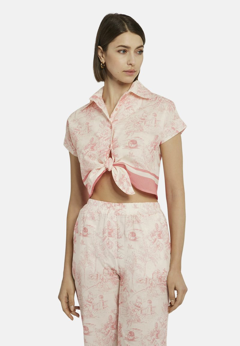 Kurzärmliges, rosa Hemd mit Kragen und einem geknoteten Front, das ein detailliertes Toile-Muster aufweist. Kombiniert mit passenden Hosen, die einen stimmigen Look erzeugen.