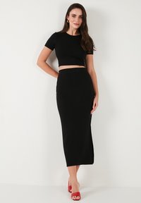 Top scurt negru, ajustat, cu mâneci scurte, asociat cu o fustă lungă neagră, cu o fante pe lateral. Modelul poartă sandale cu toc roșii.