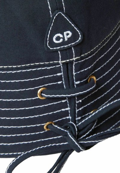 Cappello a secchiello in tessuto nero con design a righe bianche, occhielli dorati e chiusura con laccio. Presenta una toppa con il logo "CP".