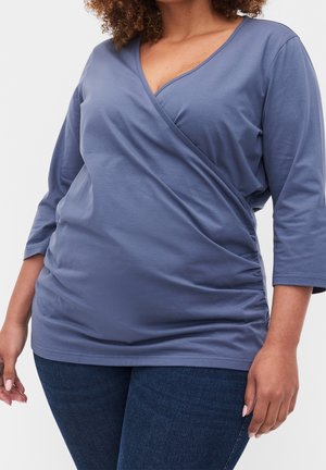 Haut style cache-coeur bleu à manches longues en jersey de coton doux, avec un col en V et des détails froncés sur les côtés pour une silhouette et une texture.