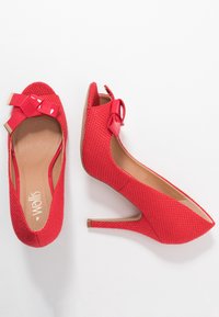 Chaussures à talons hauts rouges avec une tige en tissu texturé, bout ouvert et un accent de nœud brillant à l'avant. Talon aiguille étroit et semelle intérieure beige.
