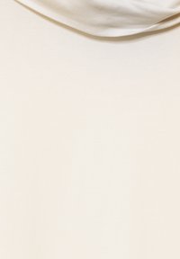 T-shirt crème avec une texture douce et lisse et un décolleté drapé. Le tissu semble extensible et léger, idéal pour un usage décontracté.