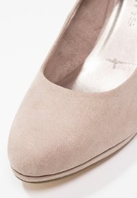 Gros plan sur une chaussure plate pour femme en suède beige avec un bout rond et une texture lisse sur fond blanc.