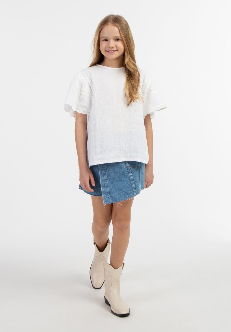 Weißes Baumwolloberteil mit Spitzenakzenten, getragen mit einem Jeansrock und cremefarbenen Cowboy-Stiefeln. Glatte Textur und legere Passform.