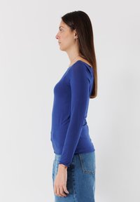 Maglietta a maniche lunghe blu con silhouette aderente e scollatura rotonda, abbinata a una gonna di jeans. Tessuto liscio, dettagli minimi.
