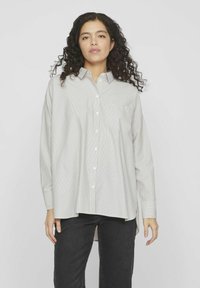 Camisa abotonada en gris claro con un patrón de rayas finas, cuenta con un bolsillo en el pecho, mangas largas y un corte holgado.