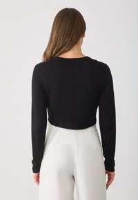 Black cropped long-sleeve top with a round neckline, smooth texture, and fitted design, paired with high-waisted white pants.